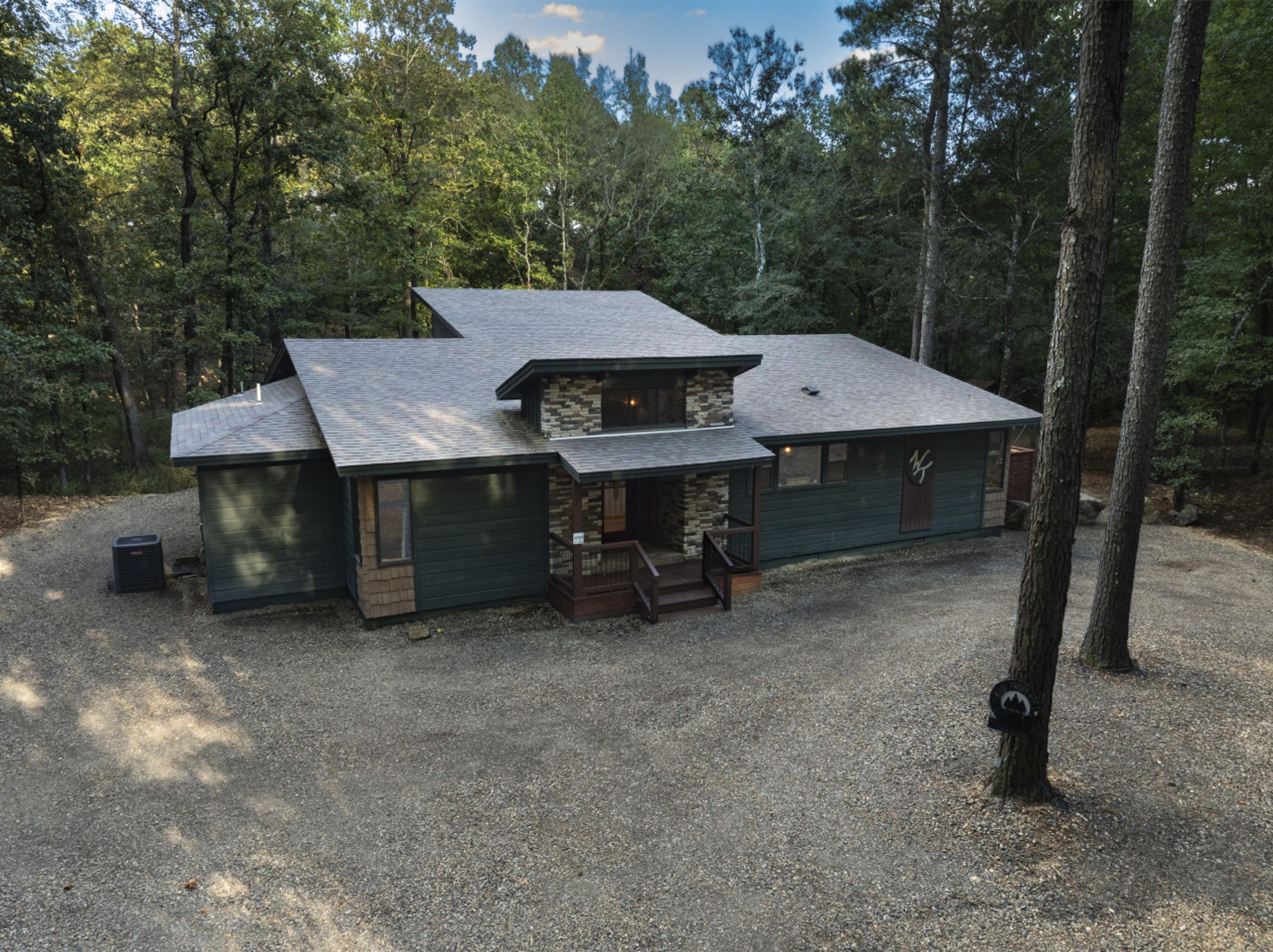 A cabin with a stone foundation, a large porch, and a gravel driveway.