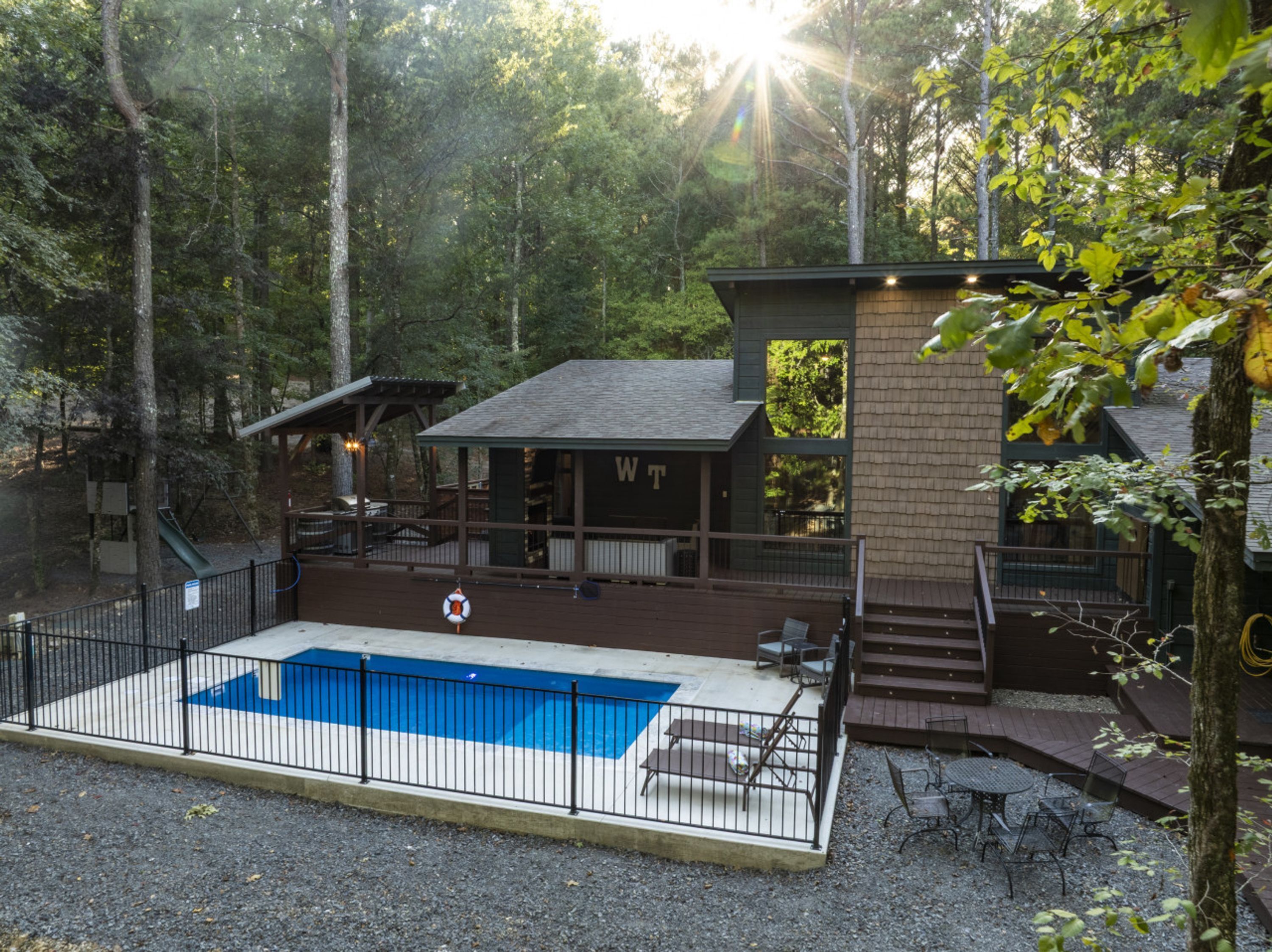 Una cabaña con piscina, rodeada de árboles.