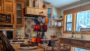 A kitchen with wooden cabinets, a granite countertop, and a hanging pot rack. - Wine Time Family Retreat With Heated Pool Hot Tub 4 King Suites Near Broken Bow (Broken Bow)