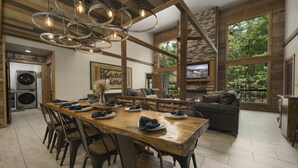 A spacious dining area with a wooden table and chairs, a stone fireplace, and a large window offering a view of the outdoors. - Wine Time Family Retreat With Heated Pool Hot Tub 4 King Suites Near Broken Bow (Broken Bow)