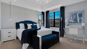 A modern bedroom with a large bed, a bedside table, a desk with a chair, and a window with curtains. - Come and Stay at the Best of Championsgate! (Davenport)