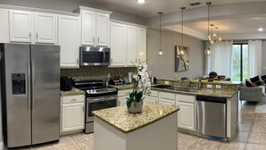A modern kitchen with white cabinets, stainless steel appliances, granite countertops, and a central island. - Come and Stay at the Best of Championsgate! (Davenport)