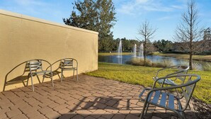 A paved patio with metal chairs, a pond with fountains, and trees in the background. - Come and Stay at the Best of Championsgate! (Davenport)