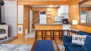 A compact living space with a kitchenette, a dining area with wooden stools, a blue sofa with a 'LOVE' pillow, and a small rug. - Ski-in Ski-out Chair 8 3rd Floor No Elevator (Brian Head)