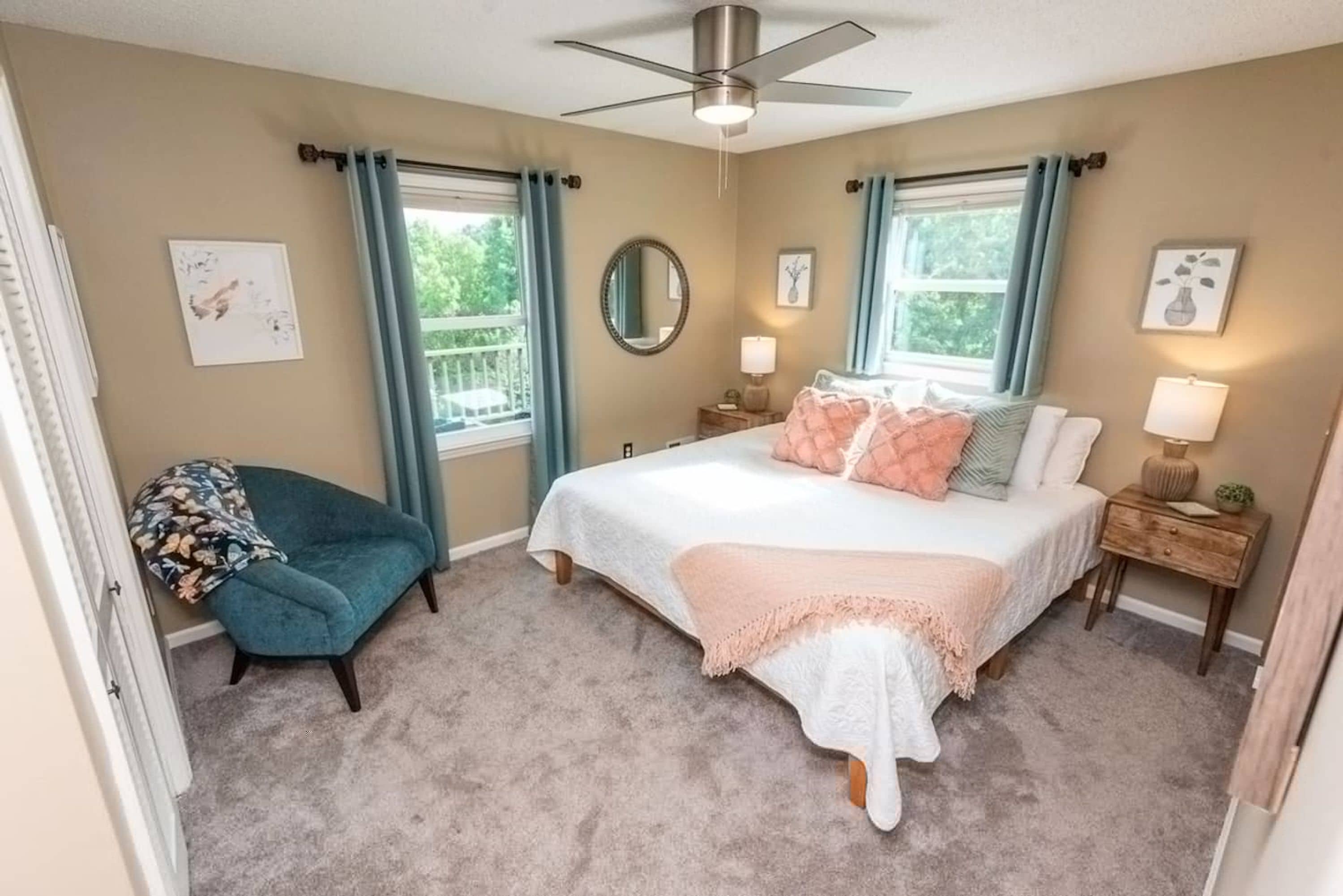 A bedroom with a bed, two bedside tables, a ceiling fan, a chair, and a window with curtains.