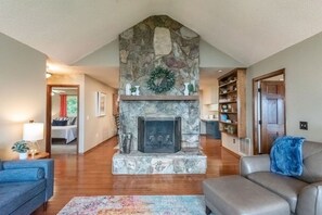 A living room with a stone fireplace, a sofa, a coffee table, and a bookshelf. - Blue Ridge Gateway Cabin With Mountain Views (Moravian Falls)