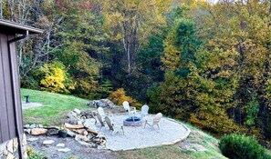 A backyard with a fire pit, outdoor seating, and a stone firewood stack. - Blue Ridge Gateway Cabin With Mountain Views (Moravian Falls)
