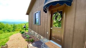 A wooden house with a stone pathway leading to a door with a 'WELCOME HOME' mat. - Blue Ridge Gateway Cabin With Mountain Views (Moravian Falls)