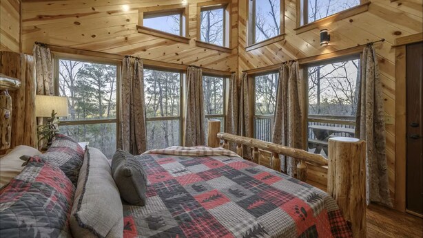 A wooden cabin interior with a bed, a nightstand, and a window with curtains. - Three Bears Hideout Luxury Mountain Cabin Getaway for Families Groups (Almont)