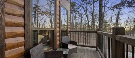 A wooden deck with wicker furniture and a glass table, overlooking a forested area.