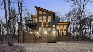 A multi-story log cabin with a staircase leading to a deck, surrounded by a forest. - Three Bears Hideout Luxury Mountain Cabin Getaway for Families Groups (Almont)