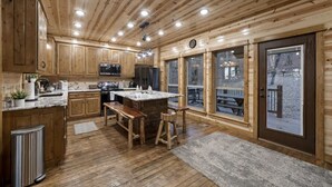 A wooden cabin kitchen with a central island, wooden cabinets, and large windows. - Three Bears Hideout Luxury Mountain Cabin Getaway for Families Groups (Almont)