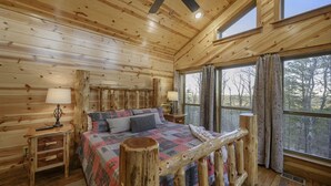 A log cabin bedroom with a bed, wooden headboard, nightstands, and a large window with curtains. - Three Bears Hideout Luxury Mountain Cabin Getaway for Families Groups (Almont)