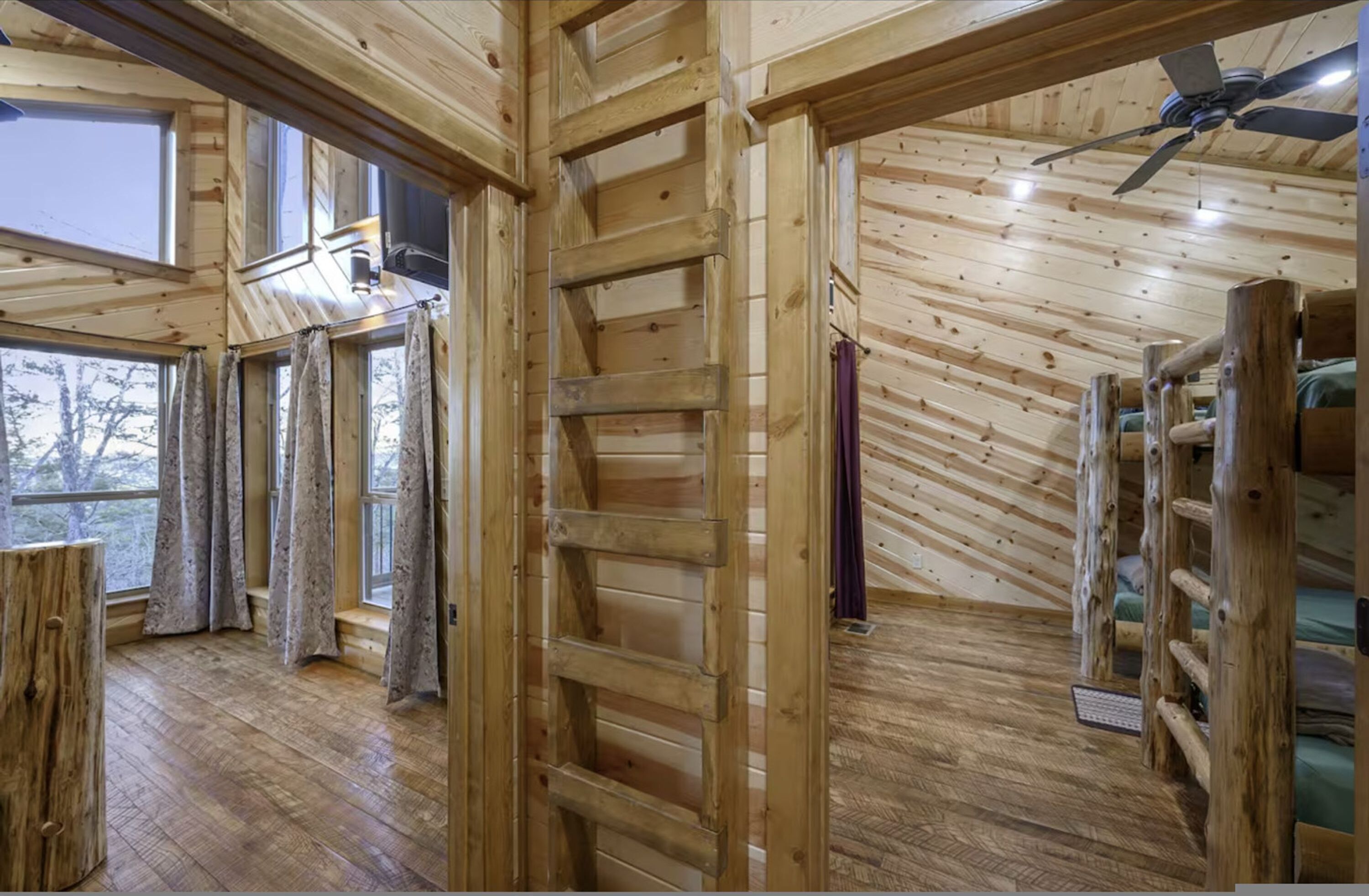 A wooden cabin interior with a loft bed, a ladder, and a ceiling fan.