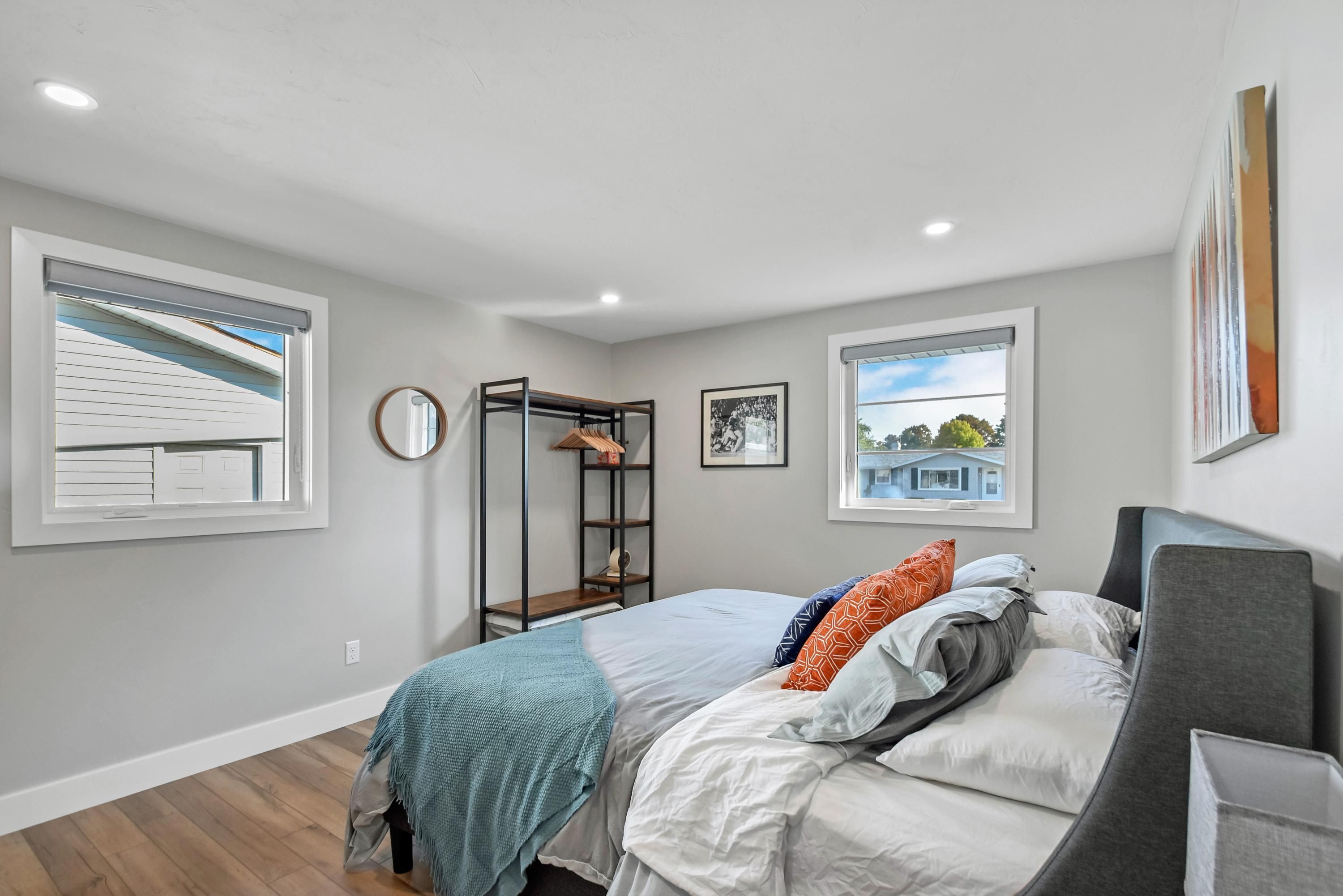 Un dormitorio con cama, armario, estantería y dos ventanas.