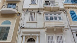 Ein mehrstöckiges Gebäude mit Balkonen, einem zentralen Eingang mit einer Tür und einer Treppe, die zum Eingang führt.