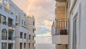 Ein mehrgeschossiges Gebäude mit Balkonen, das auf eine Straße und das Meer blickt.