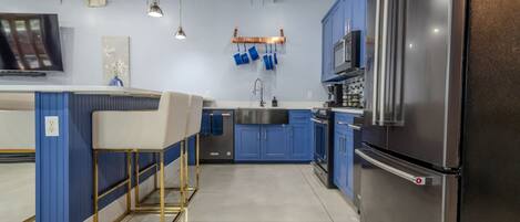 Een moderne keuken met blauwe kastjes, roestvrijstalen apparatuur en hanglampen.