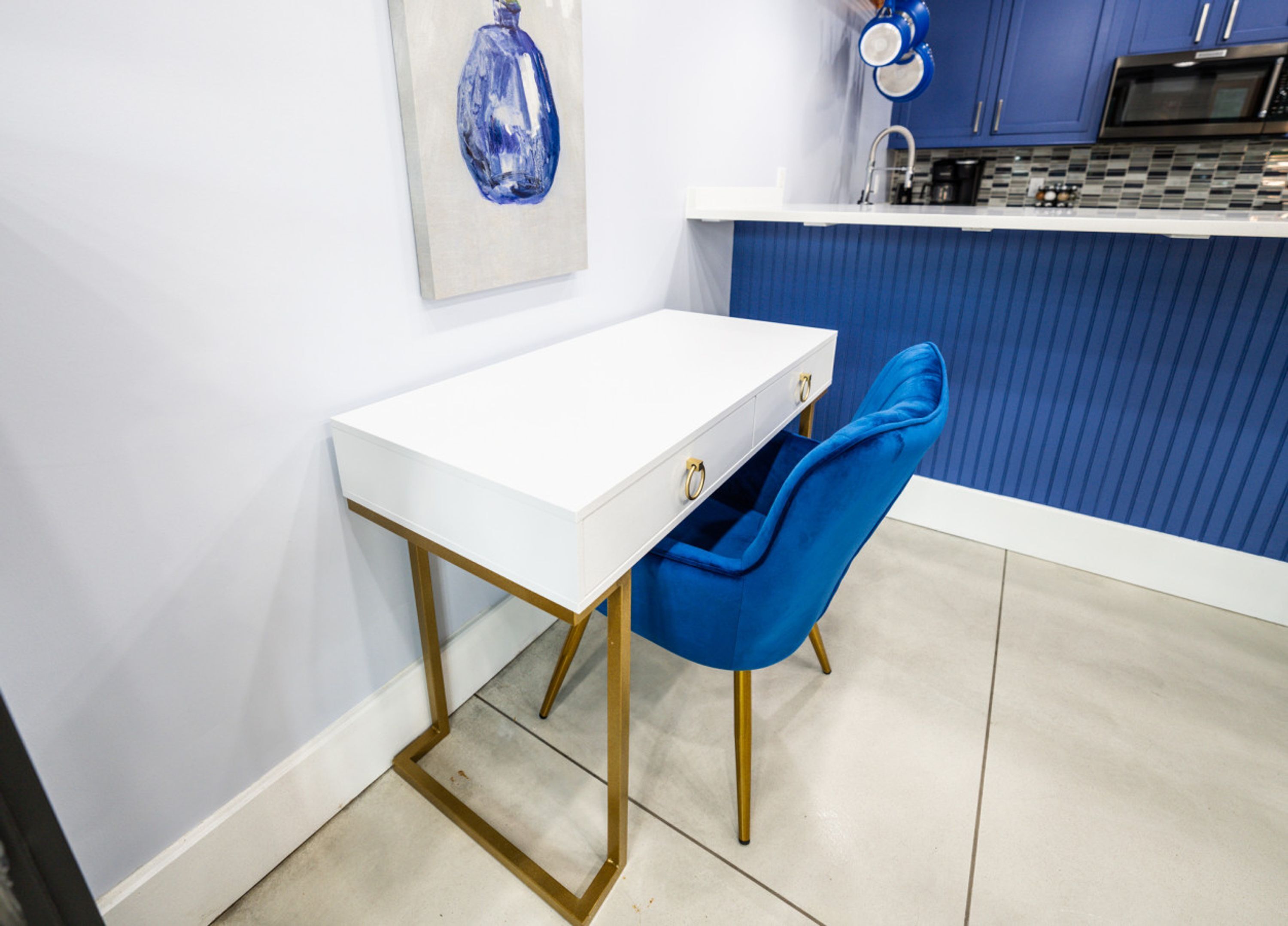 A small, modern kitchen with a white countertop, blue cabinets, and a blue chair.