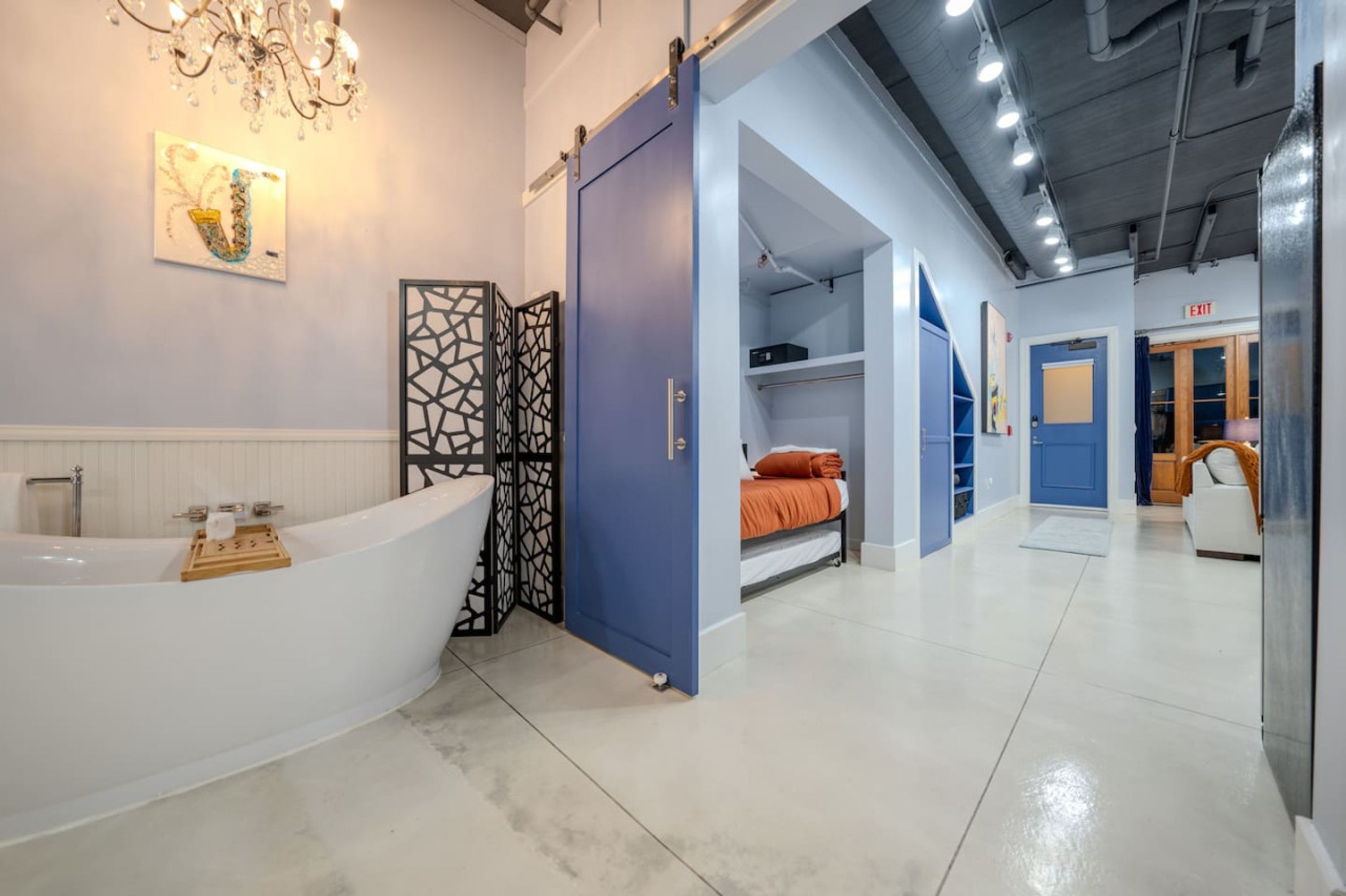 A modern bathroom with a freestanding bathtub, a shower area, and a bed in the adjacent room.