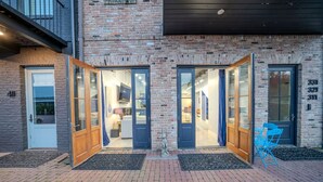 A brick building with two open doors leading to a well-lit interior, a blue chair outside, and a small statue in front. - Ground Floor Waterfront on The Rez in Madison (Madison)
