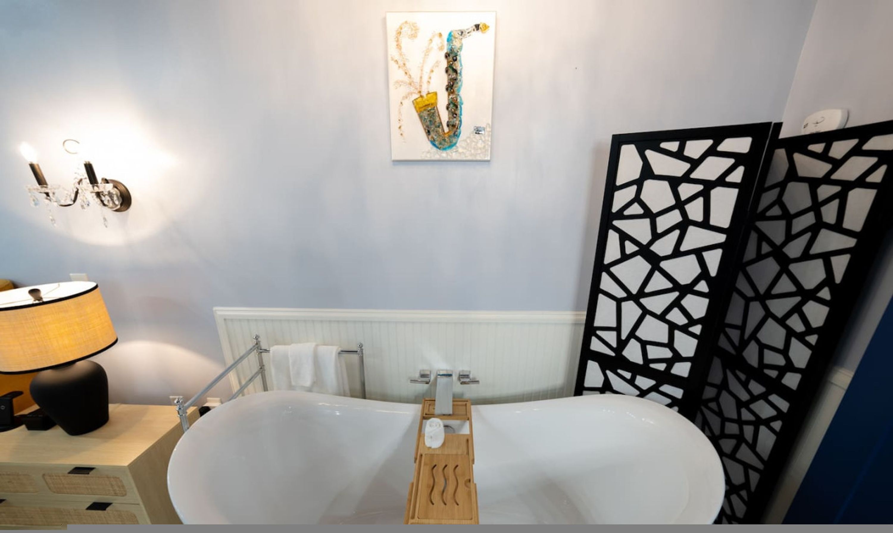 A modern bathroom with a freestanding bathtub, a towel rack, and a decorative wall piece.