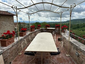 An outdoor terrace with a table and chairs, surrounded by stone walls and potted red flowers. - Tuscan Palace - Buratti Apartment (Montepulciano)