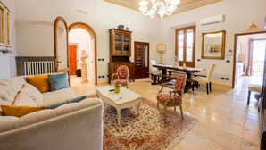 A spacious living room with a sofa, coffee table, and chairs, a dining area with a table and chairs, and a chandelier.