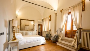 A bedroom with a bed, a chair, a dresser, a mirror, and a window with curtains.