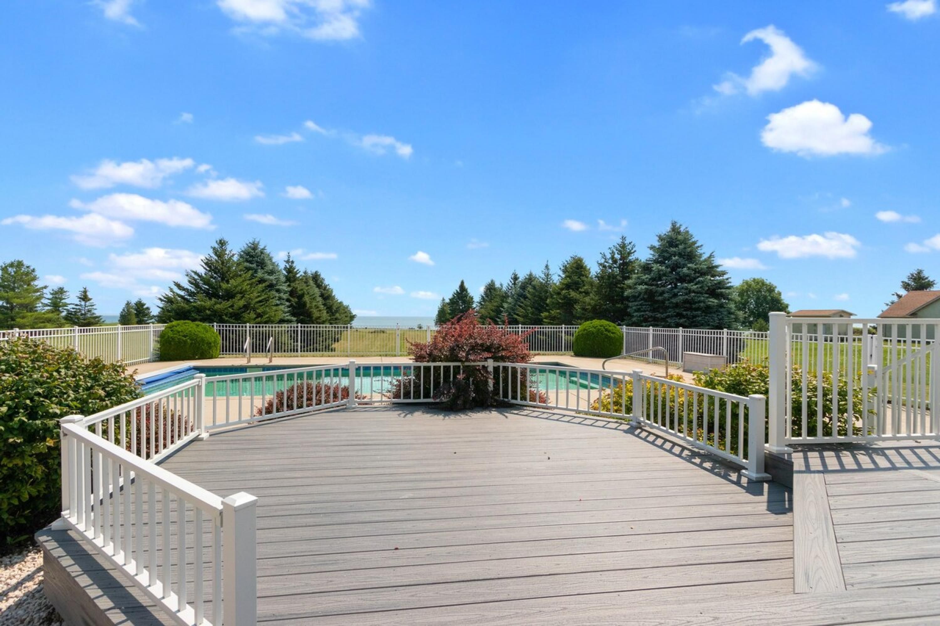 A wooden deck with a pool, surrounded by white railings and trees.
