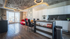 A modern kitchen with a central island, a dining area with a red sofa, and a view of the city through large windows. - Balanzone s Creative Penthouse (Msida)