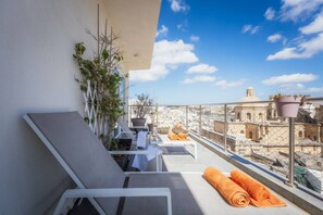 Un balcón con sillones de descanso, una mesa y plantas en macetas.