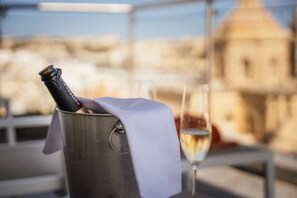 Una botella de champán en un balde de metal con un paño, una copa de champán y una vista de un edificio al fondo.