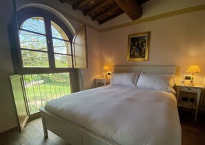 A bedroom with a large bed, two bedside tables with lamps, a painting on the wall, and a window with an open shutter. - Agriturismo Borgo Sette Tigli Apt 5 (Montepulciano)