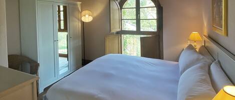 Un dormitorio con una cama grande, un armario, un ventanal con vistas y una lámpara.
