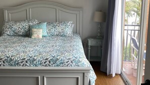 Een slaapkamer met een bed, nachtkastje, lamp en een balkon met uitzicht.