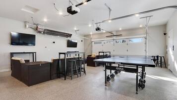 A spacious indoor area with a ping pong table, seating, and a mounted projector.