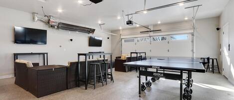 A spacious indoor area with a ping pong table, seating, and a mounted projector.