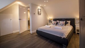 Un dormitorio con una cama grande, piso de madera y techo inclinado con iluminación empotrada.