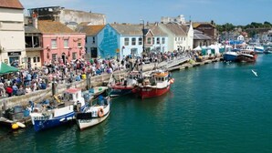 Un puerto con barcos amarrados a lo largo del muelle, edificios bordeando la orilla y una multitud de gente en la costa.