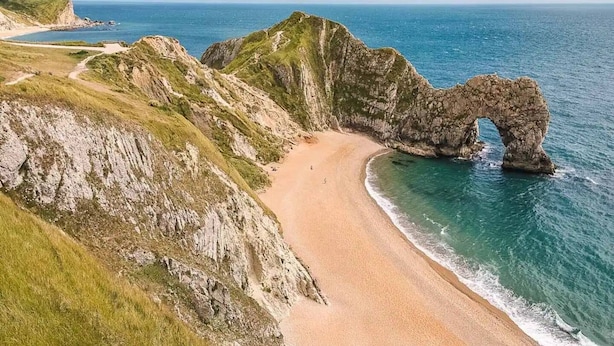 Un paisaje costero con una formación rocosa prominente en forma de arco sobre una playa arenosa.