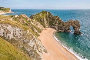 A coastal landscape with a prominent rock arch formation, a sandy beach, and a clear view of the ocean. - Best Beach Side Family Flat Central Weymouth (Weymouth)