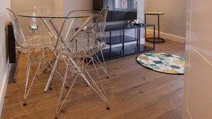 A modern living room with a glass dining table, clear chairs, a flat-screen TV, and a small side table. - Luxury Charming Seaside Flat Weymouth (Weymouth)