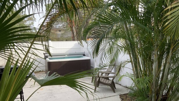 Un jardín trasero con un jacuzzi, una silla y diversas plantas.
