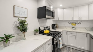 A modern kitchen with white cabinetry, a stainless steel range hood, a yellow kettle, and a wall-mounted sign that reads "This is our happy place."