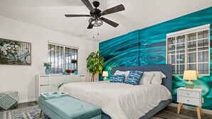 A bedroom with a bed, a ceiling fan, a window, a plant, and a nightstand.