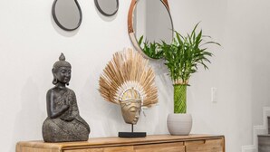 A wooden console table with a Buddha statue, a mirror, a potted plant, and a decorative headpiece.