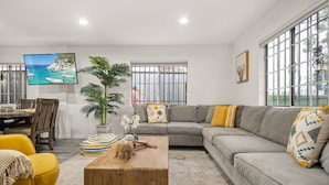 A modern living room with a grey sofa, yellow armchair, and a wooden coffee table. There is a TV mounted on the wall displaying a scenic view.