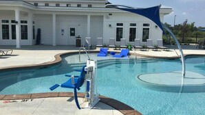 Ein Schwimmbecken mit blauen Liegestühlen, einem Liegestuhl am Pool und einem weißen Gebäude mit großen Fenstern im Hintergrund.