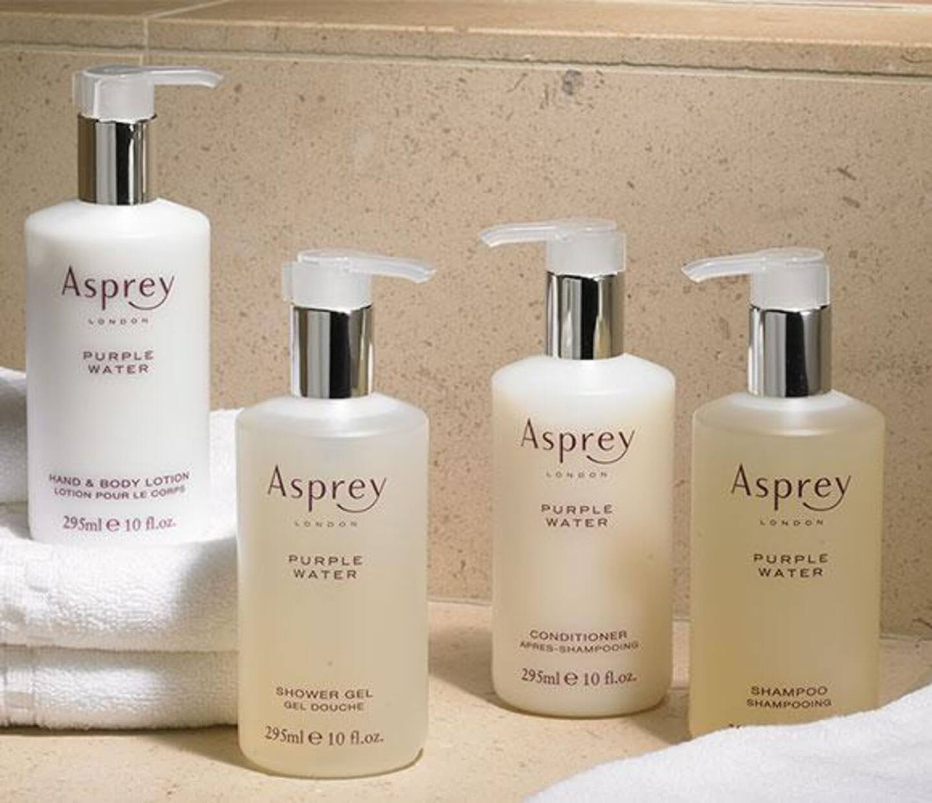 Cuatro botellas de productos Asprey Purple Water sobre una encimera.